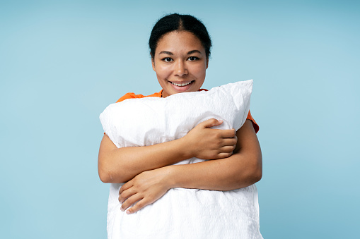 Portrait of joyful smiling african american girl holding pillow and looking at camera isolated over blue background