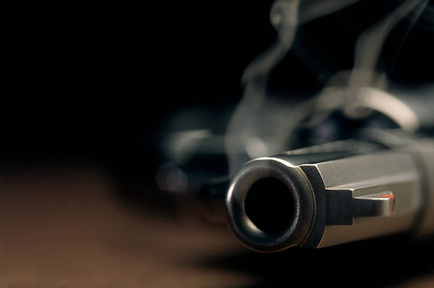 Smoking gun lying on the floor, revolver A gritty crime scene image of a smoking hand gun, revolver, lying on the floor with narrow focus on the tip if the barrel and dark background morder stock pictures, royalty-free photos & images