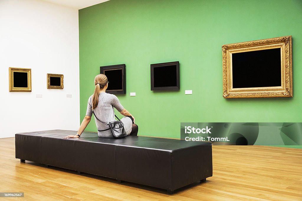Woman Sitting In Museum Woman sitting in a museum in front of antique picture frames.  Museum Stock Photo