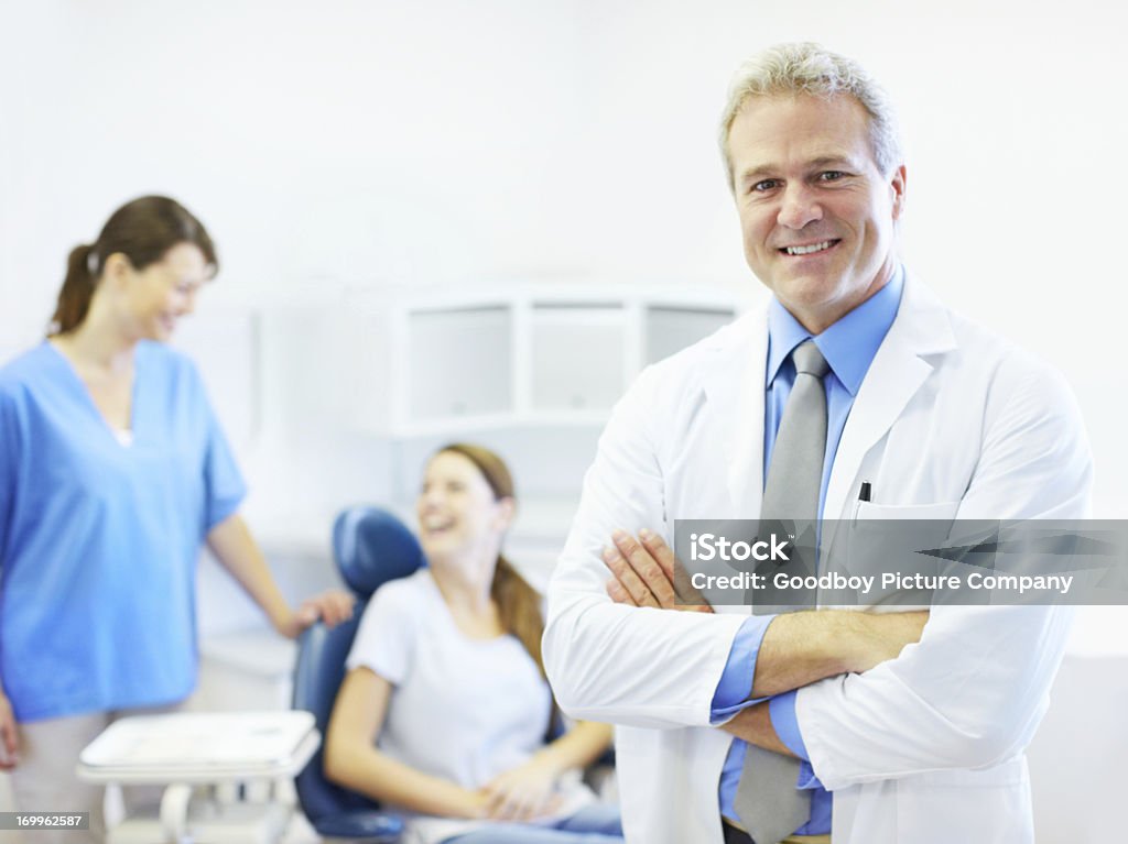 Dentista com paciente e equipe no plano de fundo - Foto de stock de Sorrindo royalty-free