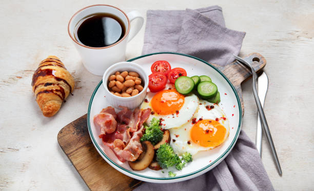 明るい背景に伝統的なエングリスの朝食プレートとベーコンストリップ、日当たりの良い面を上にした卵、野菜、ケーキ - englis ストックフォトと画像