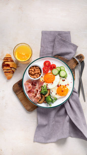 traditional englis breakfast plate with bacon strips, sunny side up eggs, vegetables and cake on light background - englis imagens e fotografias de stock