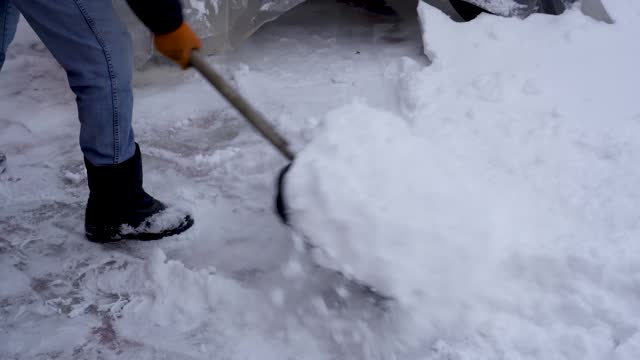 A man cleans snow in the winter in the courtyard of the house.  A man cleans the snow with a shovel