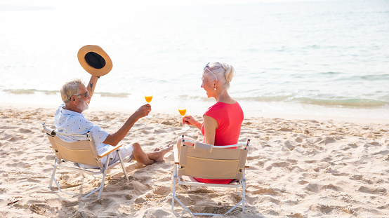 Celebrate Elderly couple man and woman celebration and drinking and looking at the sea sky sitting on chair on beach. Vacation trip summer holiday. Party, Holiday, Summer, Friendship
