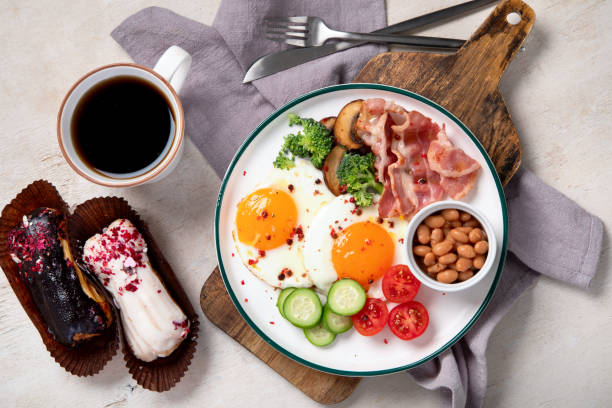 明るい背景に伝統的なエングリスの朝食プレートとベーコンストリップ、日当たりの良い面を上にした卵、野菜、ケーキ - englis ストックフォトと画像