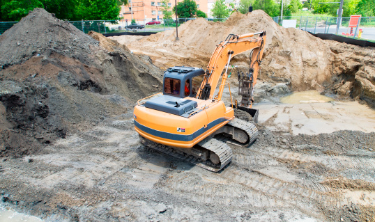 A large construction excavator removes contaminated soil from an urban brownfield development site.