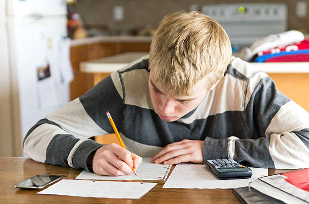 Teen Male Doing Homework at Kitchen Table A late teenaged male high school student doing math homework at a kitchen table. math homework stock pictures, royalty-free photos & images