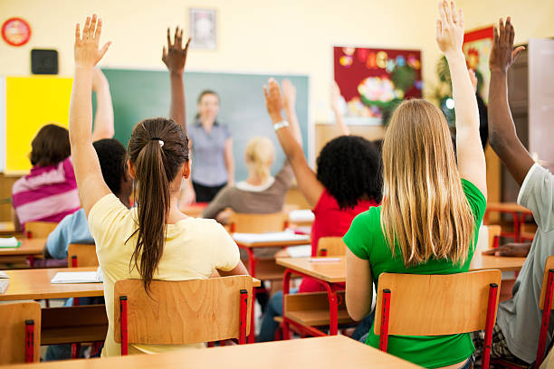 istock Group of teenagers sitting in classroom with raised hands. 169972290