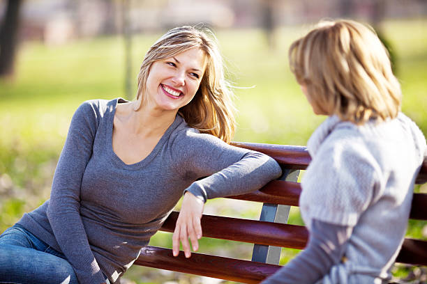 Two cheerful beautiful women sitting on the bench in the park and having a conversation.
