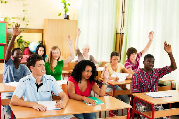 Group of teenagers sitting in the classroom with raised hands Cheerful teens sitting in the classroom and raising hands to answer on the question.   teenage high school girl raising hand during class stock pictures, royalty-free photos & images