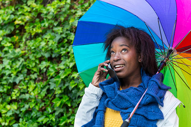 utilizzo di cellulari sotto la pioggia - candid women african descent umbrella foto e immagini stock