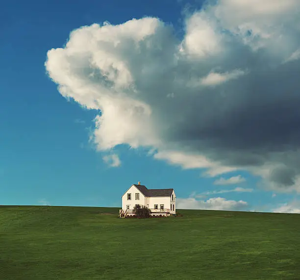 A farm house sits high on a hill under imposing rain clouds.