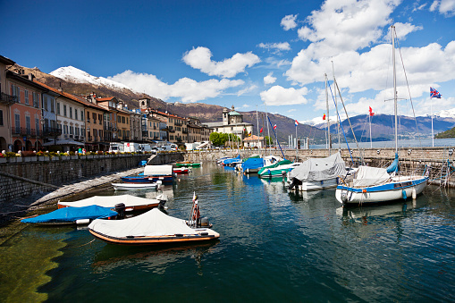 Leisure boats are moored in the small harbour of Cannobio, Italy, on the Lago Maggiore while unrecognizable people are promenading along the quay on a fresh spring day.