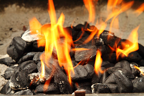 A pile of barbecue briquettes or charcoal is starting to heat up in the first flames after being lit.