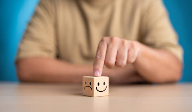 istock Man hand points on a wooden cube with happy smile face on bright side and unhappy face on dark side of wooden block cube for a positive mindset selection. Emotional state and mental health concept. 1699774685