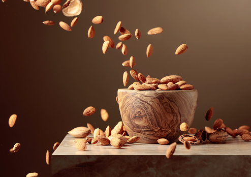 Almond nuts are poured into a wooden bowl. Brown background with copy space.
