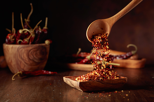 Chilli flakes are poured into a wooden dish. Chilli flakes and dried chili peppers on an old wooden table.
