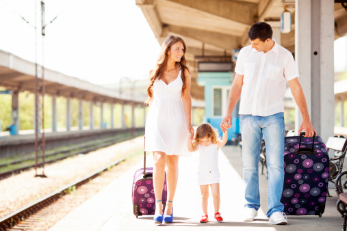 Young Cheerful Family Waiting for Train at train station. They are traveling with her 3 year old daughter. Easter Europe standard train station. They are walking and carry suitcases at train station.