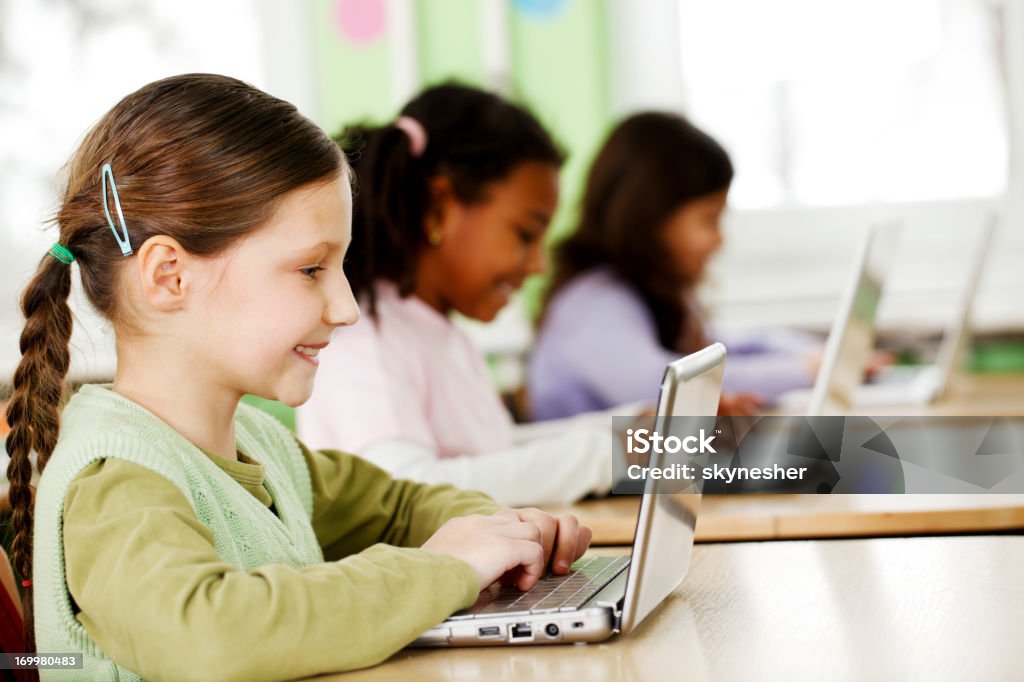 Tre sorridenti ragazze utilizzando il computer portatile in Aula. - Foto stock royalty-free di Computer