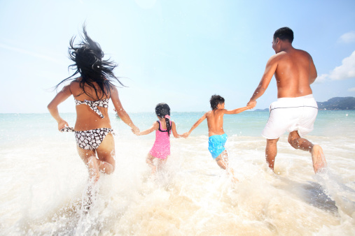 By holding each other hands Asian family enters the sea.  