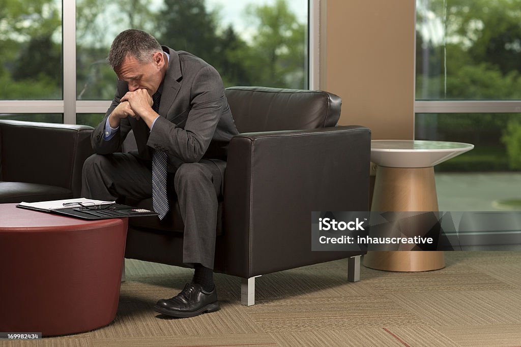 Empresário sentando, inclinando-se para frente, com as Mãos na Cabeça - Foto de stock de 50 Anos royalty-free