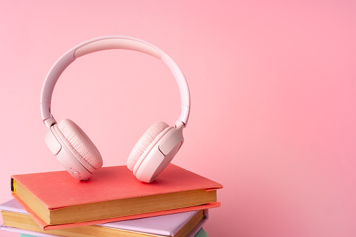 Pink headphones on a book on blue background close up