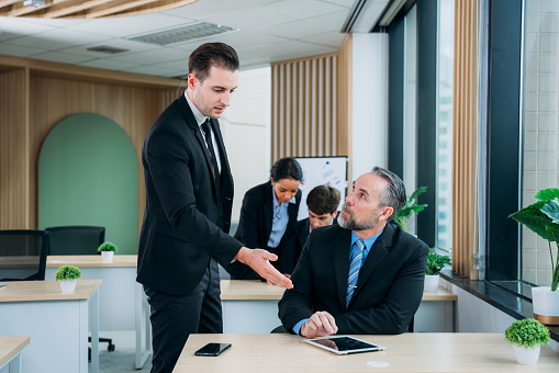 Group of people applauding speech of their colleague while sitting at table during conference