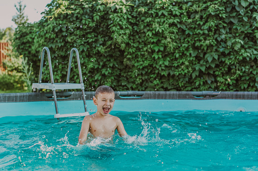 Little boy swims in the pool at their summer cottage. Back yard vacations concept.