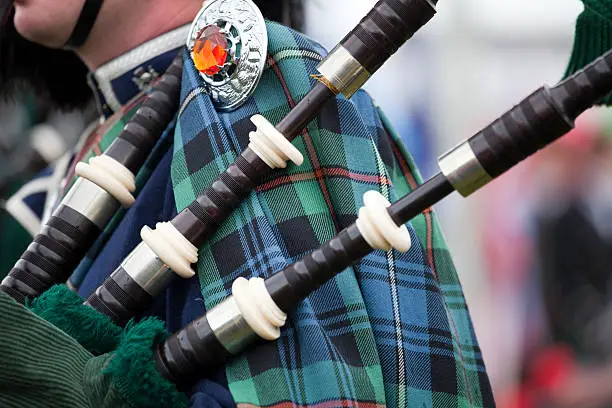 A bagpipe player wearing a traditional Scottish tartan fly plaid and plaid brooch.