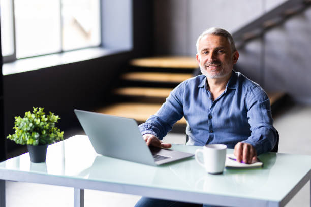 istock Mature man using laptop on desk at home and drink coffee 1699900042
