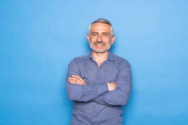 istock Handsome middle aged grey haired man standing with arms folded isolated on blue background. 1699901133