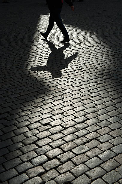 istock Mysterious Shadow Man Walks on Dark Cobblestone Background 169991028
