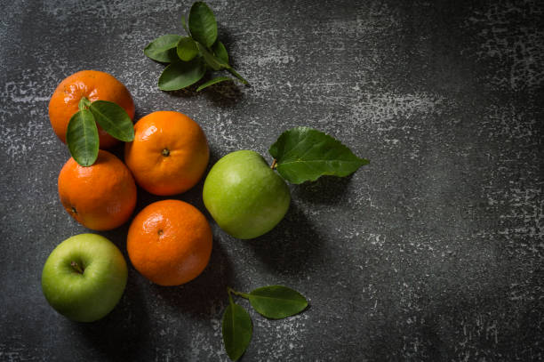 Mandarin oranges and green apples with leaves on a gray background.