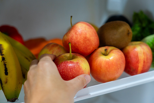 Hand picking up an apple from a fridge shelf with healthy vegan food