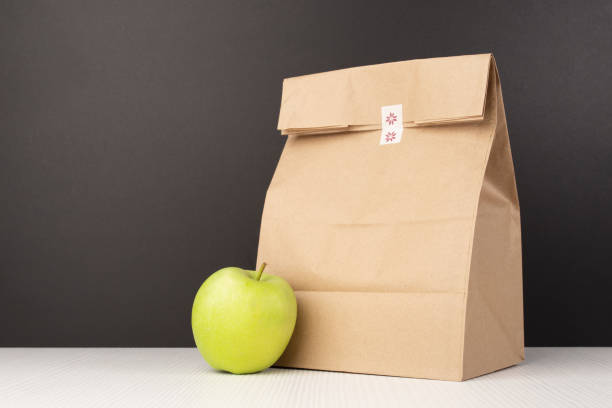 bolsa de almuerzo de papel tradicional para estudiantes con una manzana en el fondo de la pizarra - packed lunch lunch paper bag blackboard fotografías e imágenes de stock