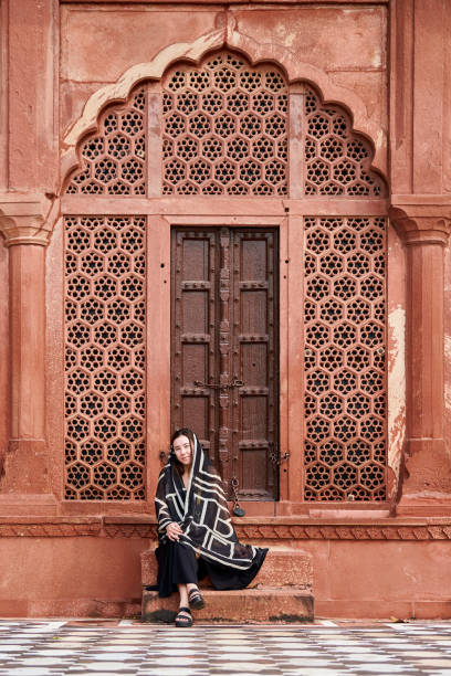 восточноазиатская женщина в черном платье сидит на ступеньках входа в индийский храм - taj mahal mahal door temple стоковые фото и изображения