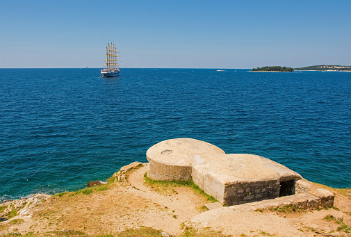 A World War Two era bunker for defending from naval attacks on the coast of Rovinj in Istria, Croatia. A tall ship is in the background