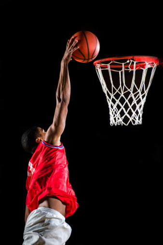 Young African-American basketball player is jumping and placing the ball in the hoop.   
