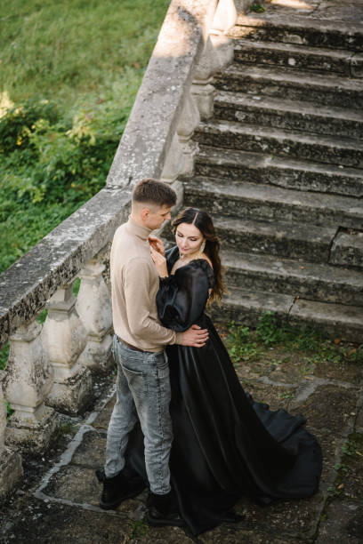 Female embrace male wall in street. Luxury couple near old Pidhirtsi Castle Ukraine. Woman in black long dress hugs man stand on stairs near ancient palace at sunset. Bride hug groom outdoor. Top view hembra abraza pared masculina en la calle. pareja de lujo cerca del antiguo castillo de pidhirtsi ucrania. mujer con vestido largo negro abraza al hombre de pie en las escaleras cerca del antiguo palacio al atardecer. abrazo de novia novio al aire libre. v