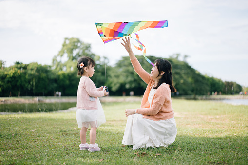 Asian mother and daughter playing kite in public park