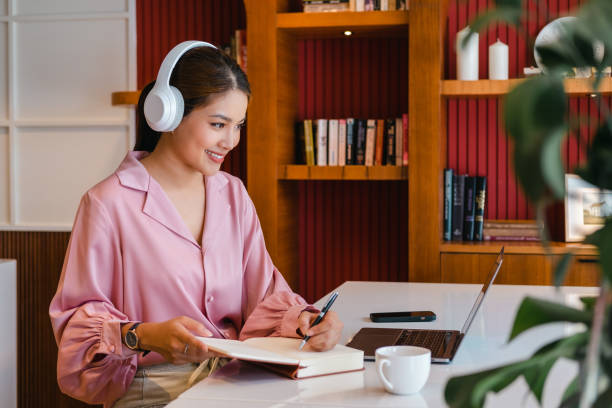 istock Smiling asian woman freelancer wearing headset communicating with client via video computer call. Concentrated student girl learning online video call via laptop computer sitting in home office . 1699953438