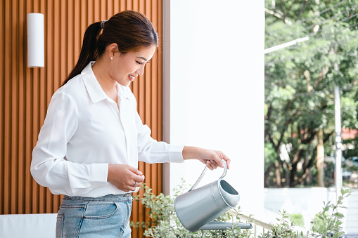 Beautiful Asian woman watering outdoor plants at home on balcony Lifestyle and concept of people who are happy with life at home.