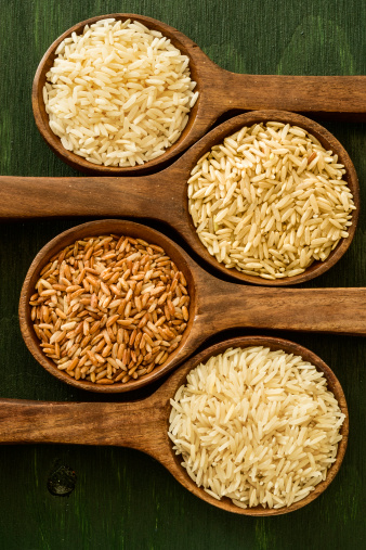Various types of rice grains in a wooden spoon placed in a row on a wood background