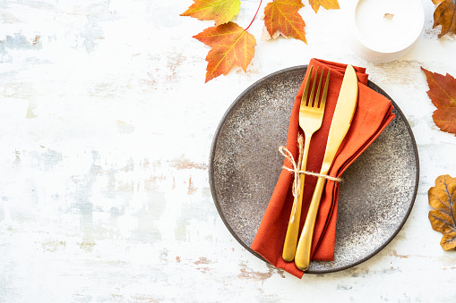 Craft plate, cutlery and autumn decorations on white background. Flat lay with copy space.