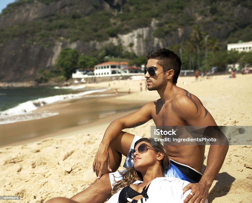 Романтический Молодая пара, сидящая на пляже наслаждаясь теплым солнцем. - Стоковые фото Пара - Человеческие взаимоотношения роялти-фри