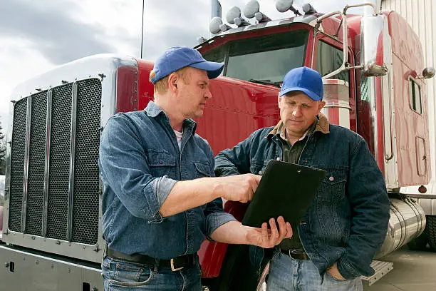 A royalty free image from the trucking industry of two truck drivers using a tablet computer at a distribution warehouse.