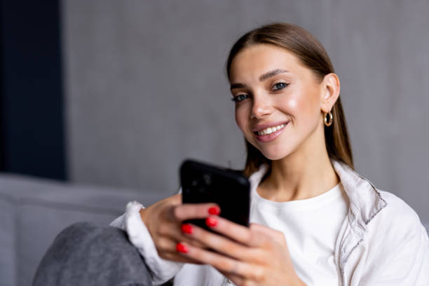 istock Happy young woman using mobile phone while sitting a couch at home 1699999188