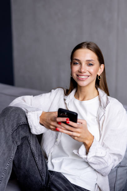 istock Happy young woman using mobile phone while sitting a couch at home 1700008018