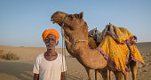 Indian man posing with camels on sand dunes, Rajasthan, India