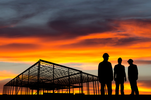 A royalty free image from the construction industry of three construction workers in front of a steel frame building having a meeting.